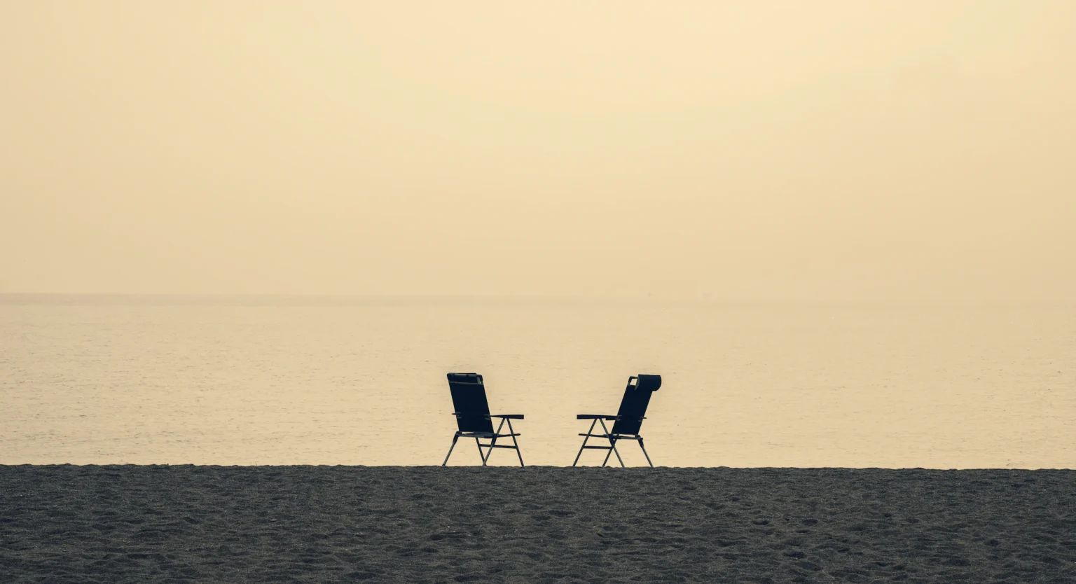 Two chairs turned toward each other on a beach at dawn